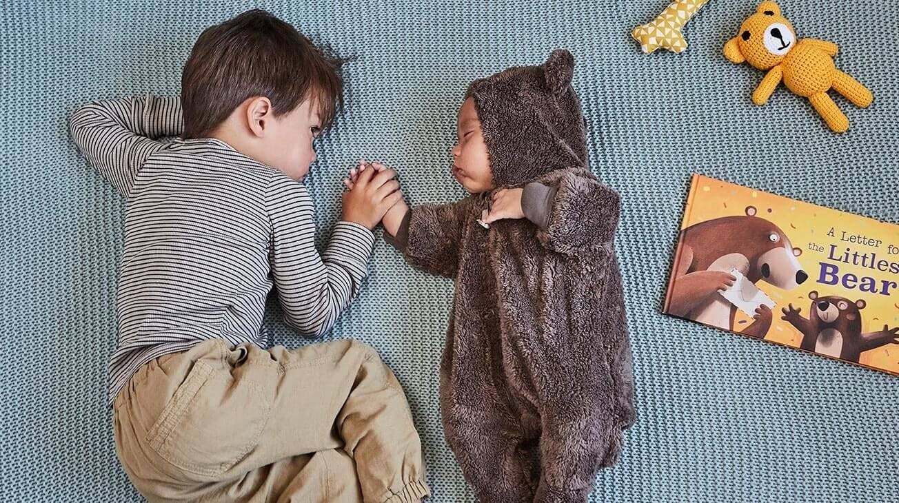 An image of the older brother holding his little brother's hand, who is dressed in a little bear outfit